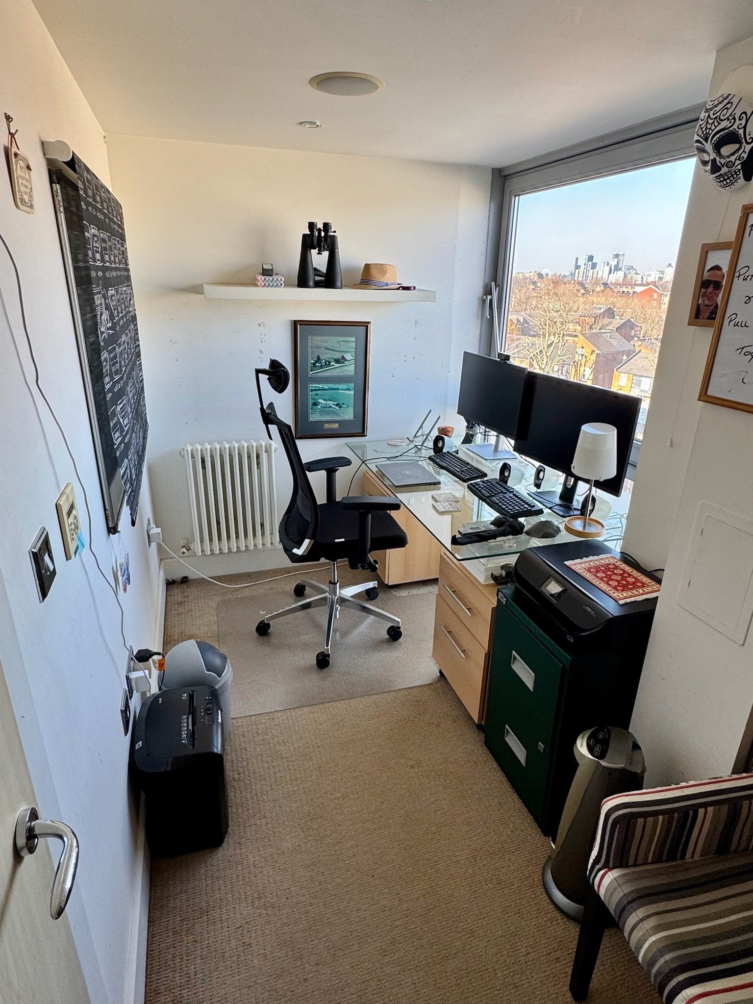 Home study with desk, twin monitors and city view through tall window